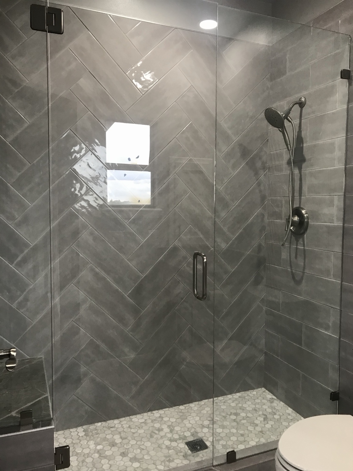 Gray herringbone tiled shower with glass enclosure